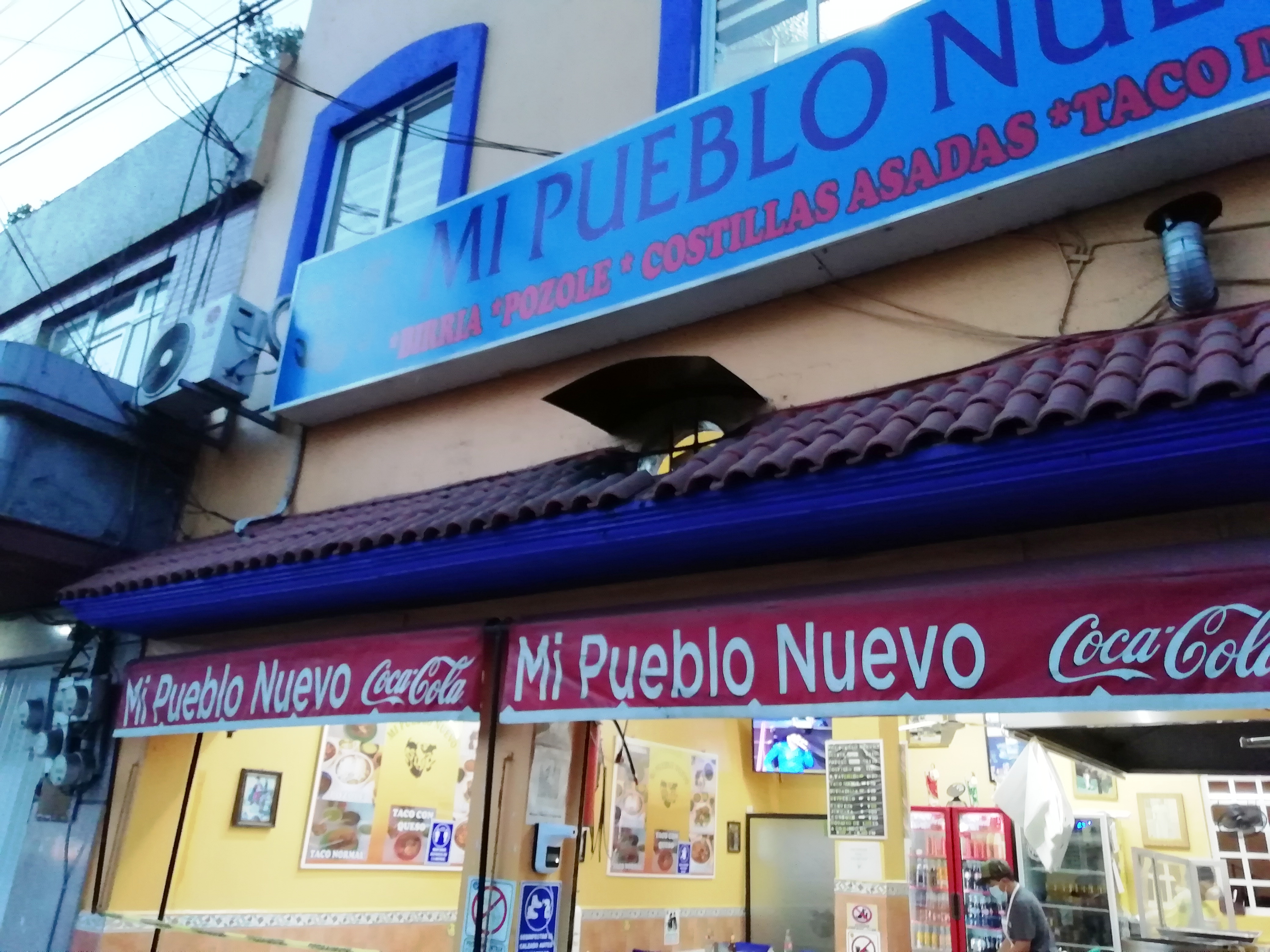 La fachada desde la banqueta: el rótulo azul de Mi Pueblo Nuevo, el tejado y el toldo rojo de la entrada