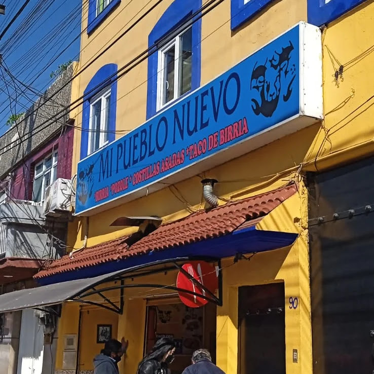 Fachada de Mi Pueblo Nuevo: rótulo azul sobre pared amarilla, tejado y toldo, en la Antigua Calzada de Guadalupe