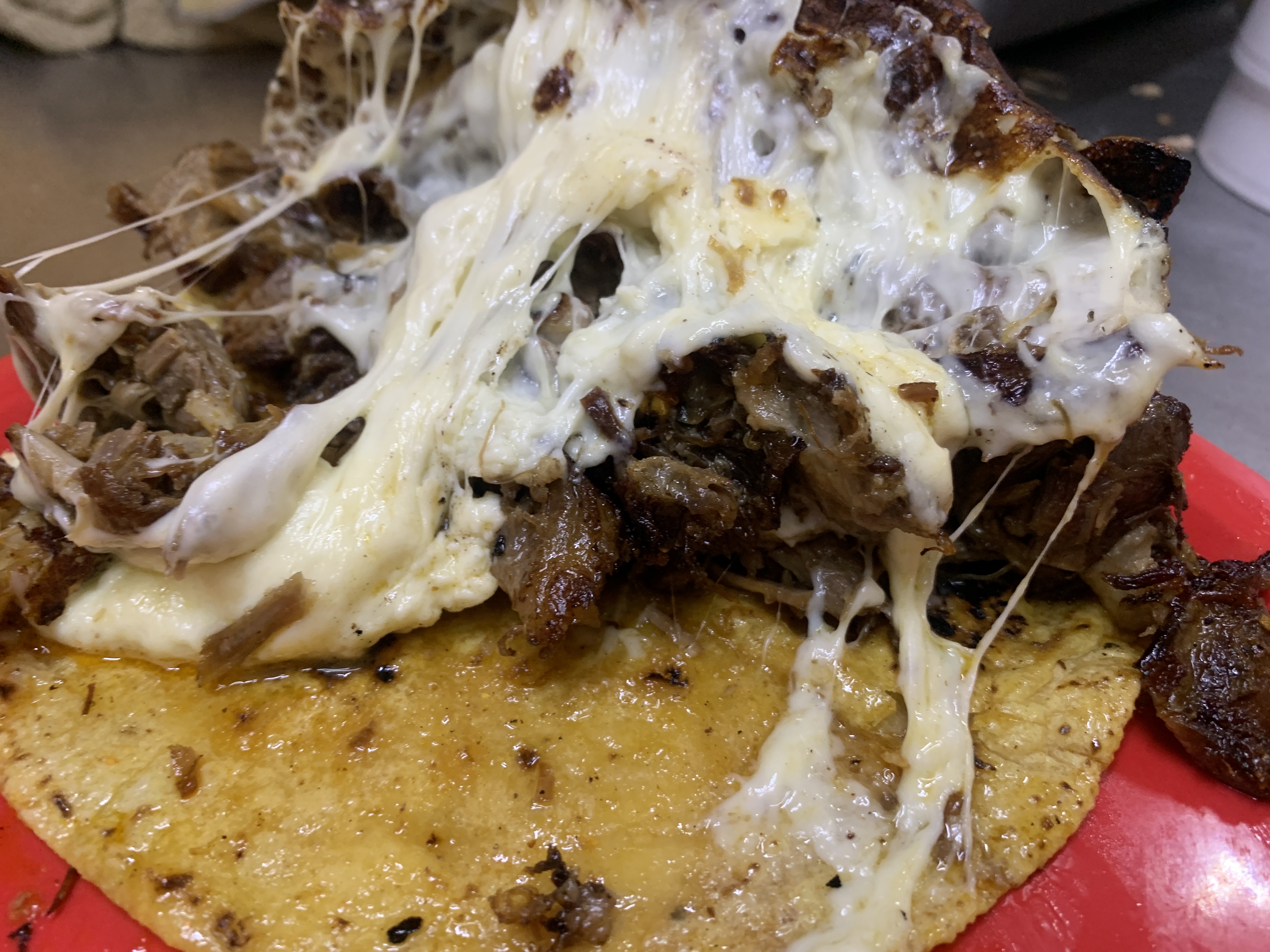 Quesabirria de cerca: tortilla dorada con birria y queso derretido escurriendo, sobre plato rojo
